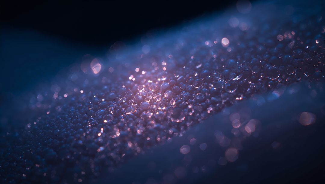 Glittering dew droplets sparkling on leaf producing bokeh and iridescent blue-purple glow