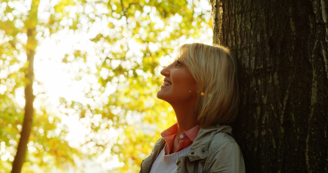 Smiling Woman Resting Against Tree in Sunny Forest - Free Images, Stock Photos and Pictures on Pikwizard.com