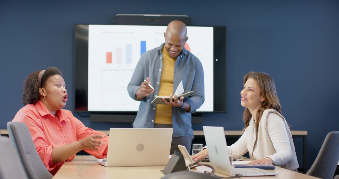 Diverse team presenting data in modern boardroom with tablet, laptops and charts