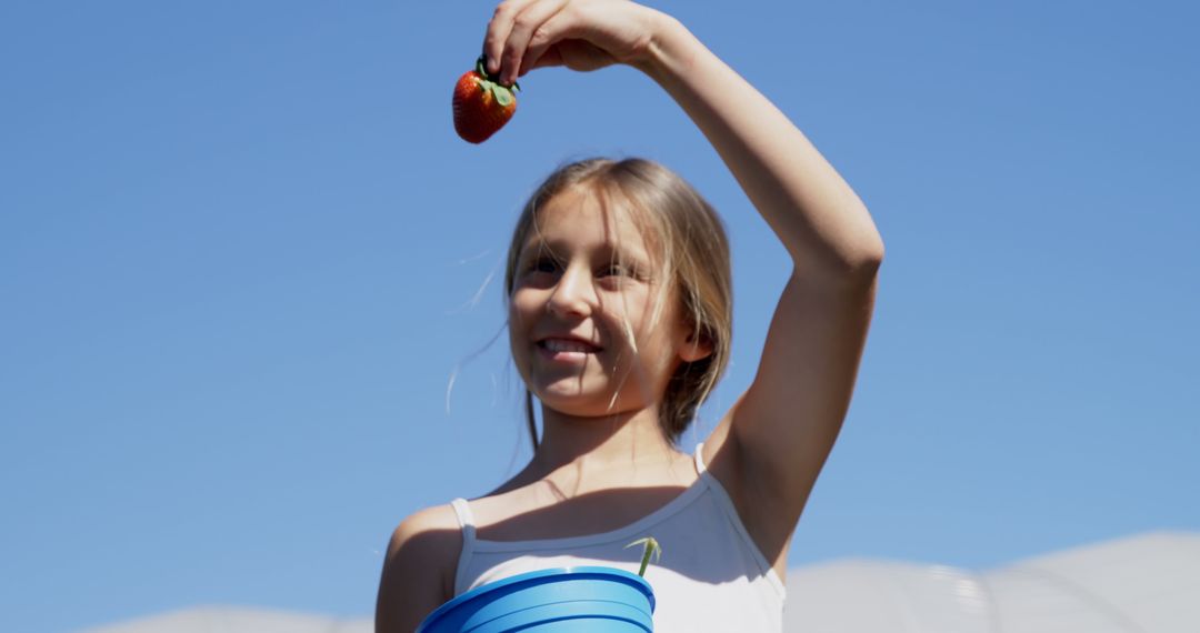Young Girl Holding Fresh Strawberry Under Clear Sky - Free Images, Stock Photos and Pictures on Pikwizard.com
