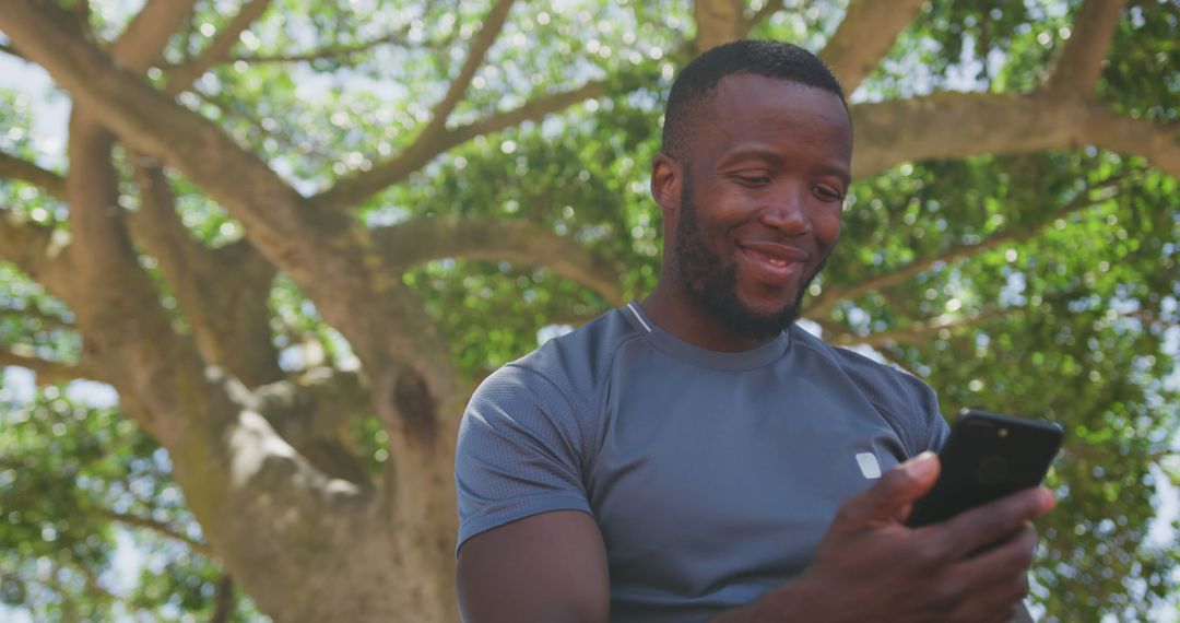 Man Smiling While Using Smartphone Outdoors Under Tree - Free Images, Stock Photos and Pictures on Pikwizard.com