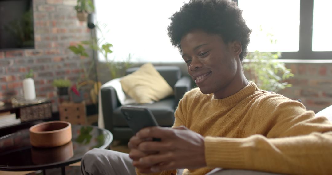 Relaxed Young Man Smiling and Texting on Smartphone in Cozy Living Room - Free Images, Stock Photos and Pictures on Pikwizard.com