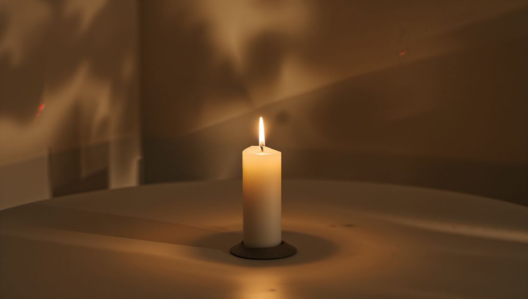 Flickering Pillar Candle Casting Warm Amber Glow and Soft Shadows on Minimal Tabletop