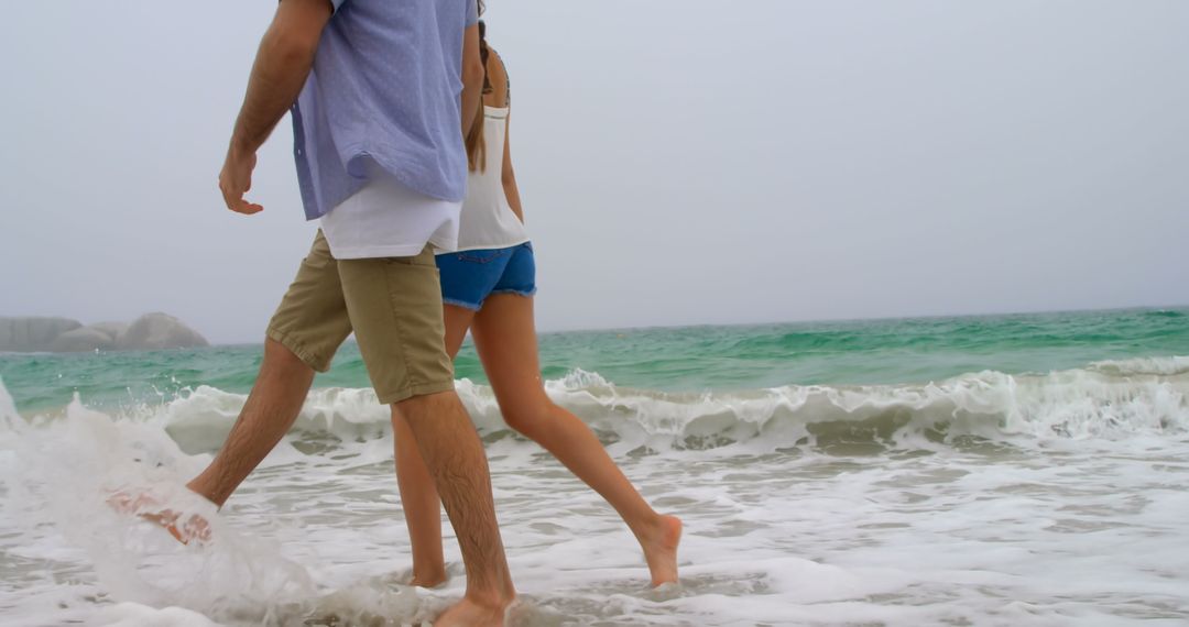 Young Couple Enjoying a Walk on Sandy Beach with Crashing Waves