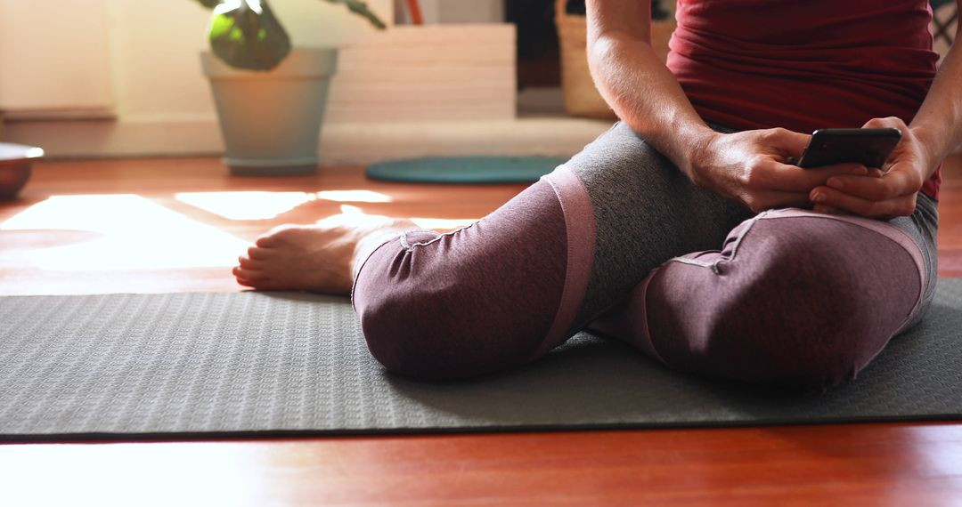 Woman Relaxing on Yoga Mat with Smartphone in Cozy Home Environment - Free Images, Stock Photos and Pictures on Pikwizard.com