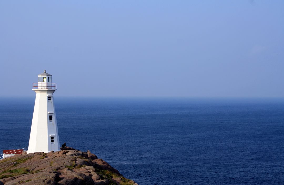 Solitary white lighthouse standing on rocky coastline by calm blue ocean - Free Images, Stock Photos and Pictures on Pikwizard.com