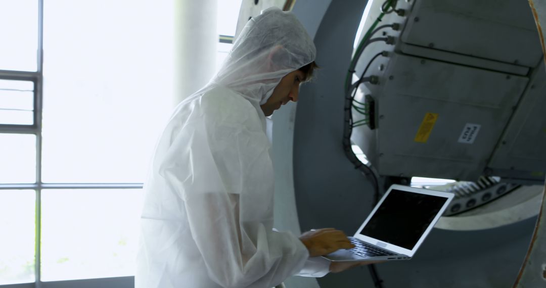 Engineer in Protective Suit Working on Laptop in Industrial Setting - Free Images, Stock Photos and Pictures on Pikwizard.com