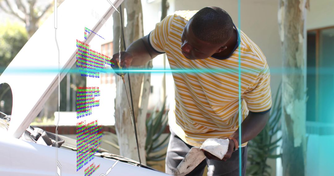 Leaning man wiping dipstick while checking engine oil under open hood in driveway