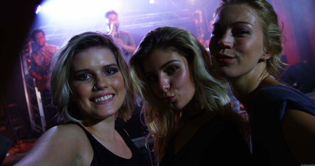 Three young women joyfully take a selfie at a concert, basked in vivid stage lights. - Free Images, Stock Photos and Pictures on Pikwizard.com