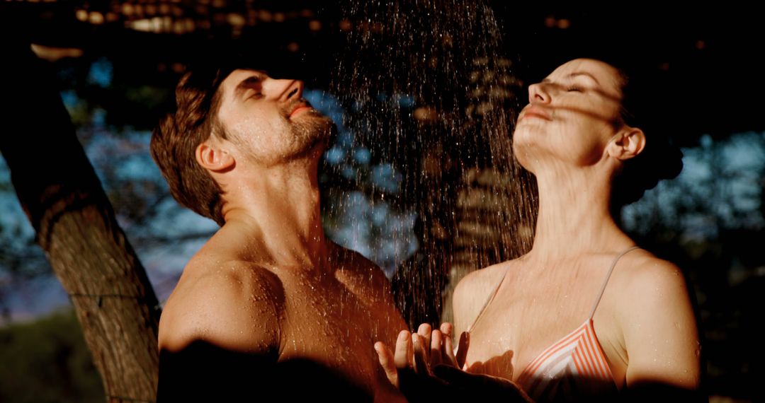 A couple finds joy and relief from summer heat under an outdoor water sprinkle. - Free Images, Stock Photos and Pictures on Pikwizard.com