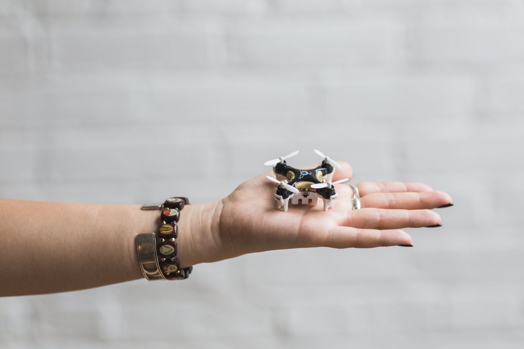 Hand Displaying Tiny Drone Against White Brick Background