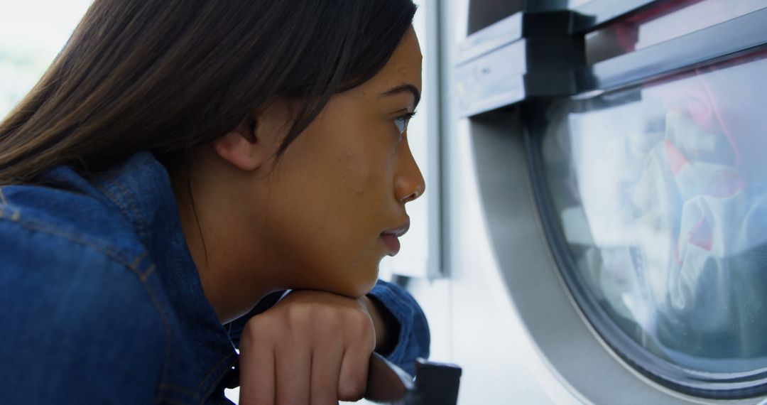 Woman Watching Clothes Spin in Washing Machine at Laundromat - Free Images, Stock Photos and Pictures on Pikwizard.com