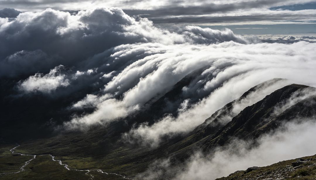 Rolling cloud waterfall cascading over rugged mountain ridge during alpine inversion