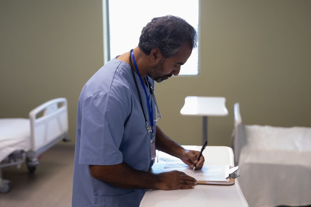 Biracial Male Doctor Writing on Clipboard in Hospital Ward - Free Images, Stock Photos and Pictures on Pikwizard.com