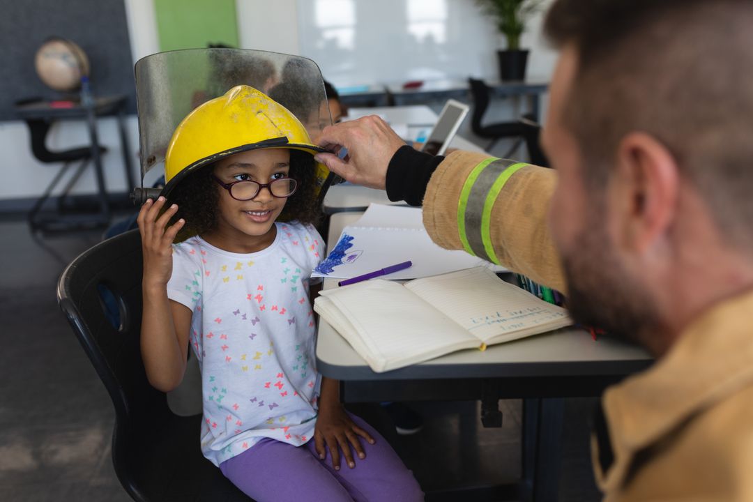 Firefighter Helping Schoolgirl Wear Helmet in Classroom - Free Images, Stock Photos and Pictures on Pikwizard.com