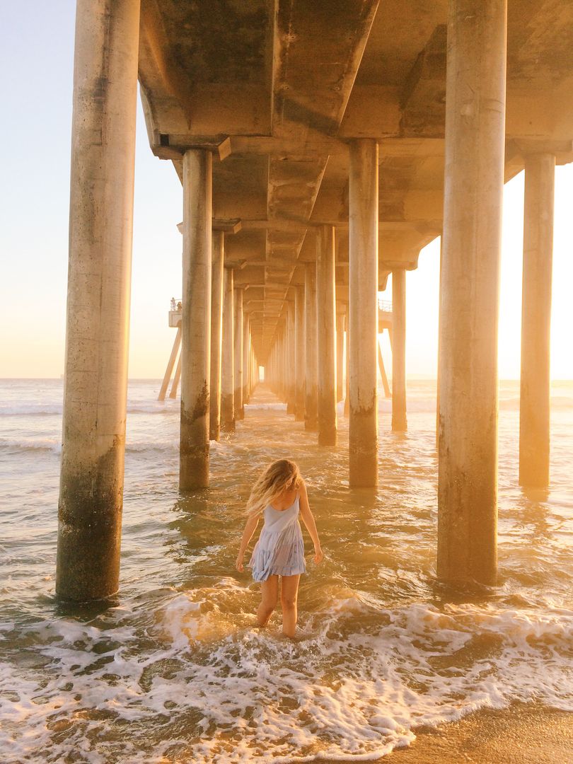 Woman Walking in Ocean Beneath Bridge at Sunset - Free Images, Stock Photos and Pictures on Pikwizard.com