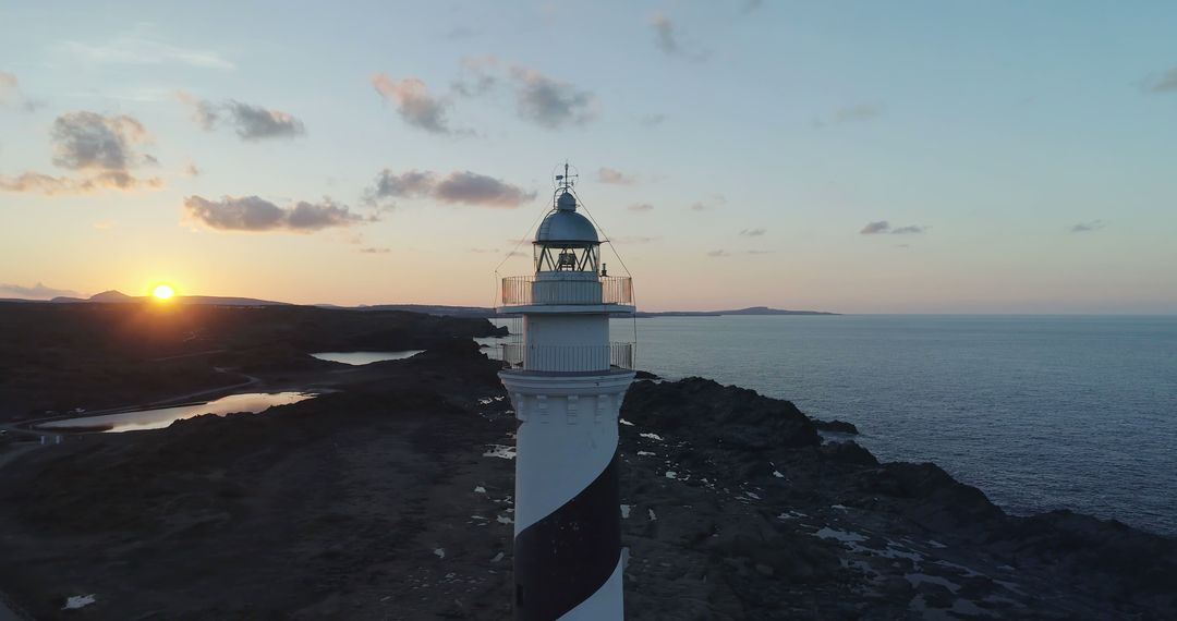 Aerial View of Black and White Striped Lighthouse at Sunset by Rocky Coastline - Free Images, Stock Photos and Pictures on Pikwizard.com