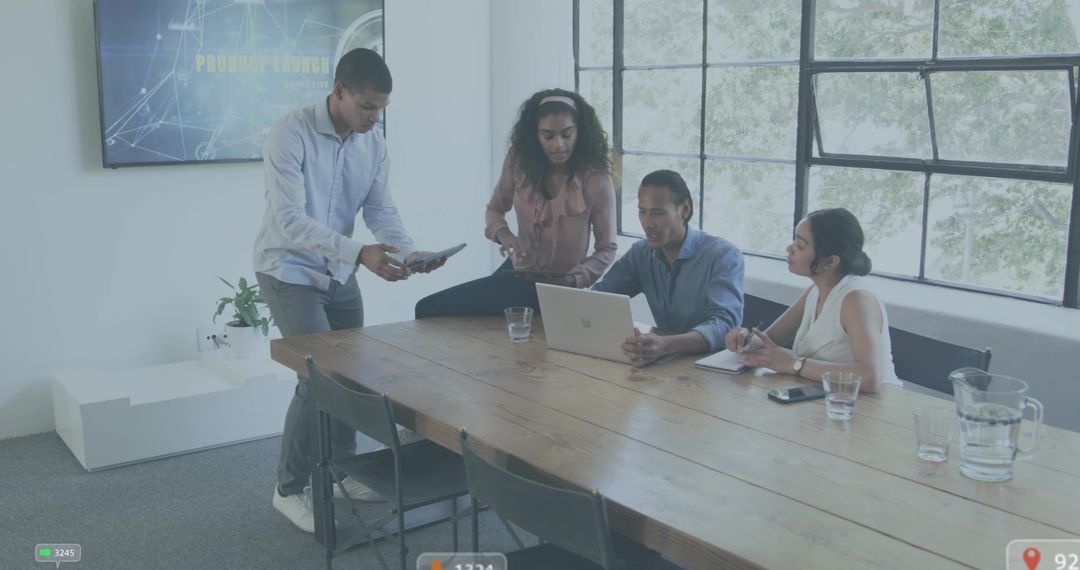 Collaborating team reviewing laptop and tablet in modern conference room with large windows