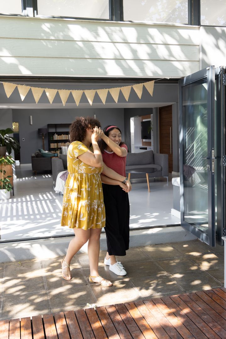 Friends Whispering on Home Patio Beneath Pennant Banner