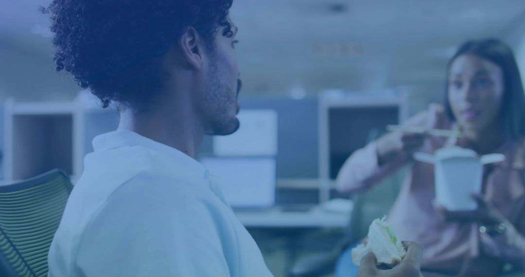 Casual office lunch conversation between coworkers sharing food in open-plan workspace