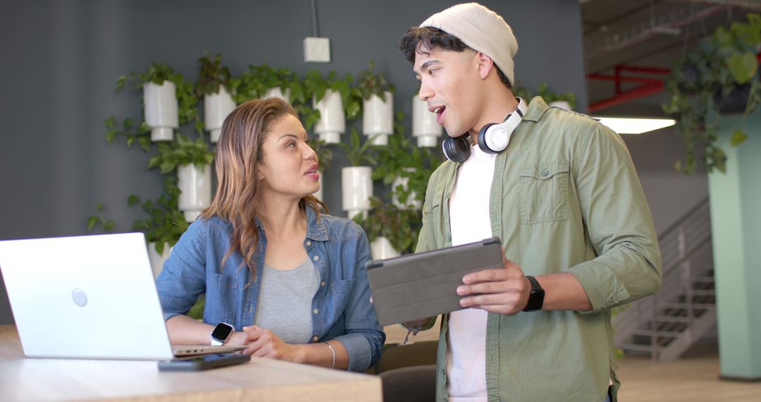 Diverse coworkers collaborating at open-office counter with laptop, tablet and living wall