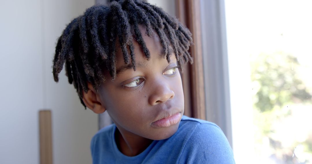 Pensive Young Boy with Dreadlocks Looking Out Window in Blue Shirt - Free Images, Stock Photos and Pictures on Pikwizard.com