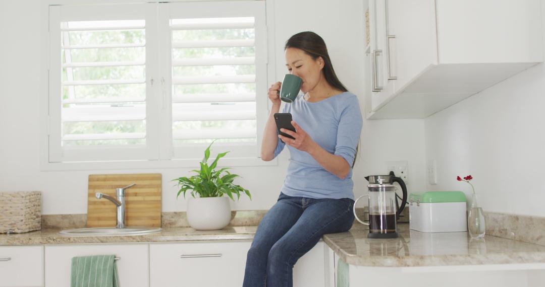 Woman Enjoying Morning Coffee and Reading Smartphone in Bright Kitchen - Free Images, Stock Photos and Pictures on Pikwizard.com