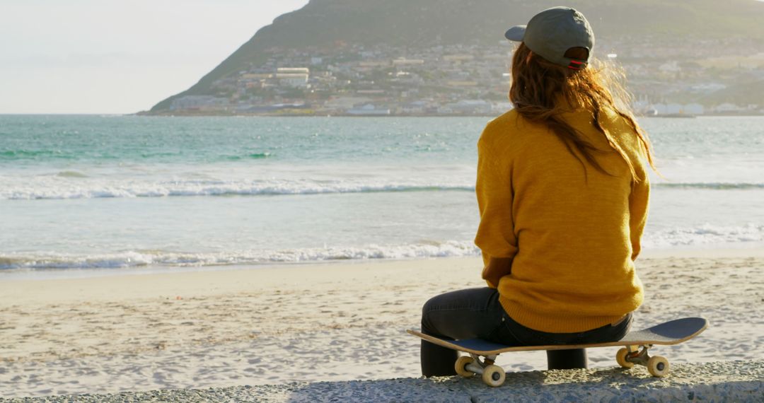 Young Woman Sitting on Skateboard by Beach Watching Ocean - Free Images, Stock Photos and Pictures on Pikwizard.com