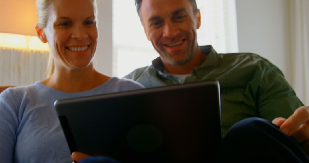 Happy Middle Aged Couple Enjoying Digital Tablet on Sofa at Home