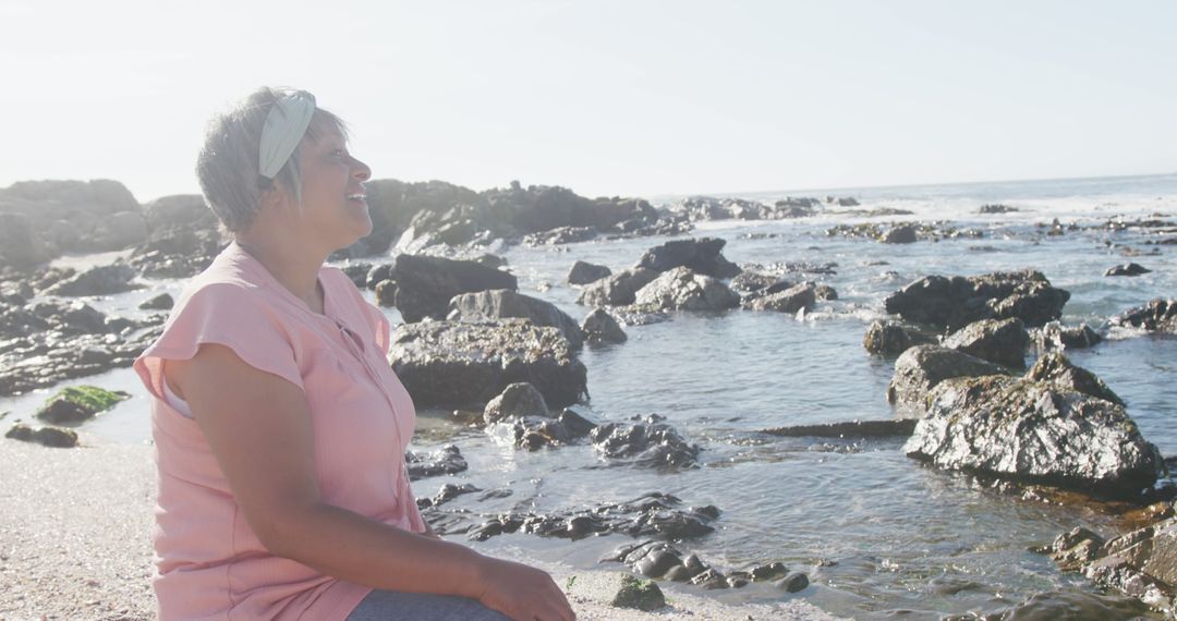 Woman Enjoying a Peaceful Moment by the Rocky Seashore - Free Images, Stock Photos and Pictures on Pikwizard.com