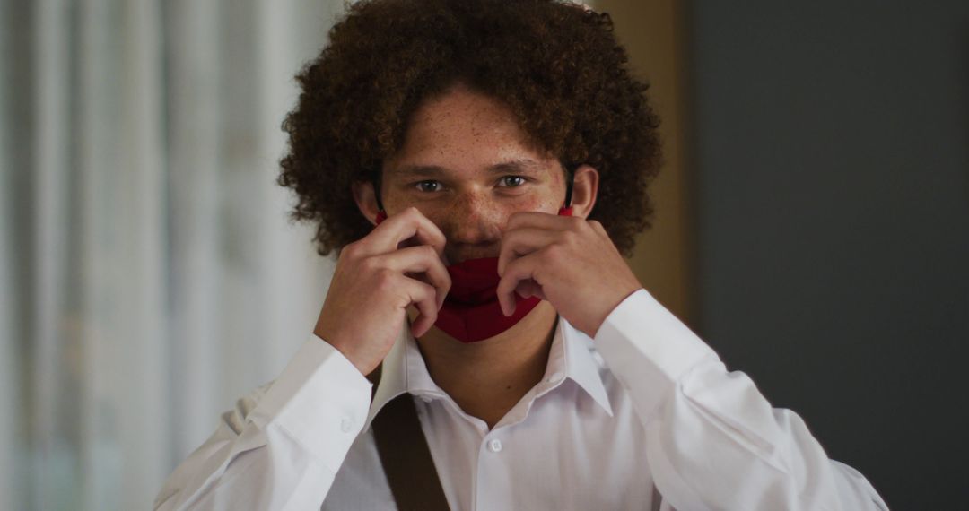 Portrait of biracial man with curly hair putting on red face mask - Free Images, Stock Photos and Pictures on Pikwizard.com