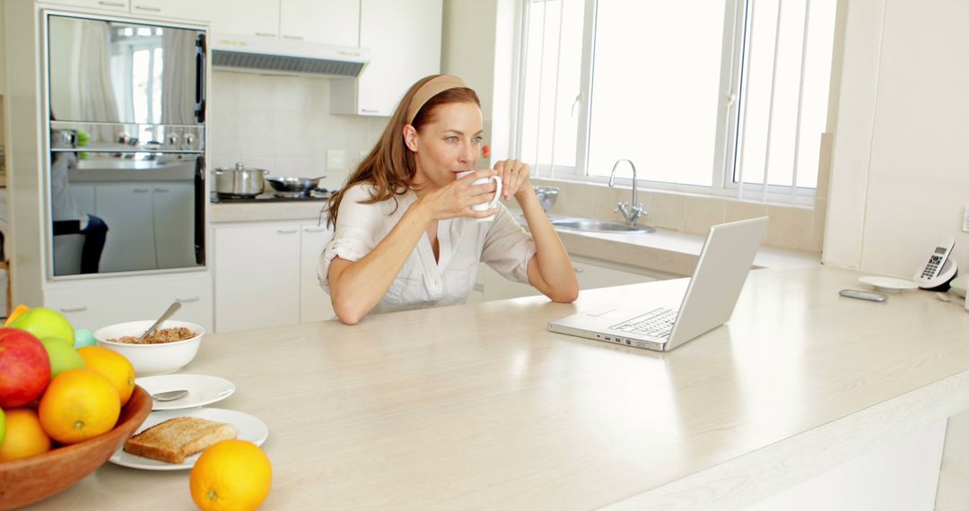 Woman Drinking Coffee While Working on Laptop in Modern Kitchen - Free Images, Stock Photos and Pictures on Pikwizard.com