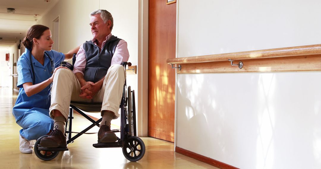 Nurse Offering Support to Elderly Man in Wheelchair in Hospital Corridor - Free Images, Stock Photos and Pictures on Pikwizard.com