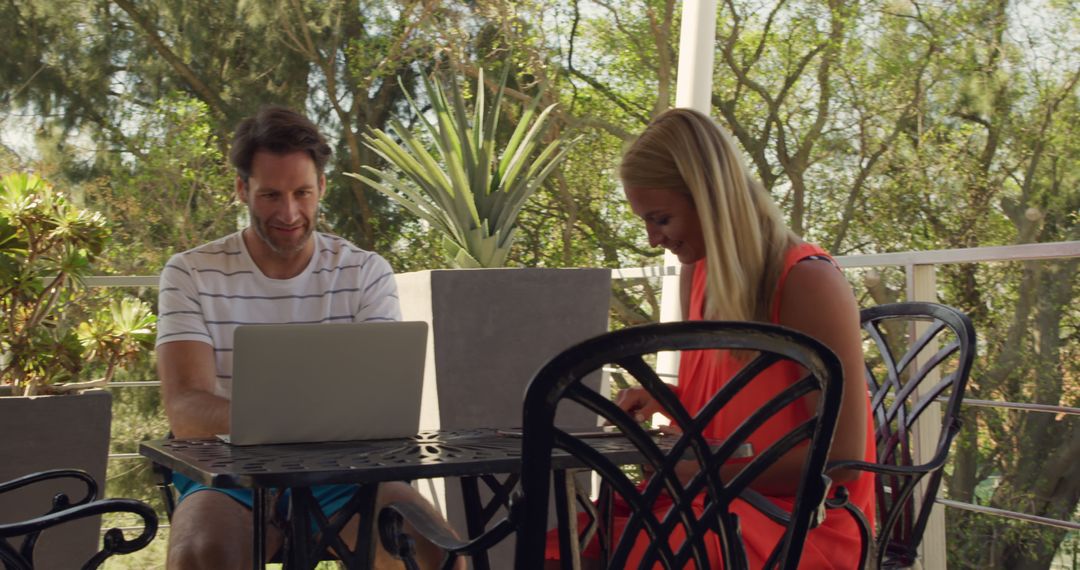 Couple Enjoying Relaxing Outdoors with Laptops in Sunny Resort Setting