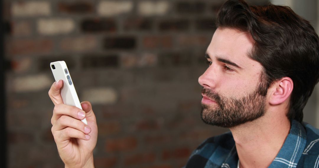 Man Concentrating on Smartphone with Brick Wall Background - Free Images, Stock Photos and Pictures on Pikwizard.com