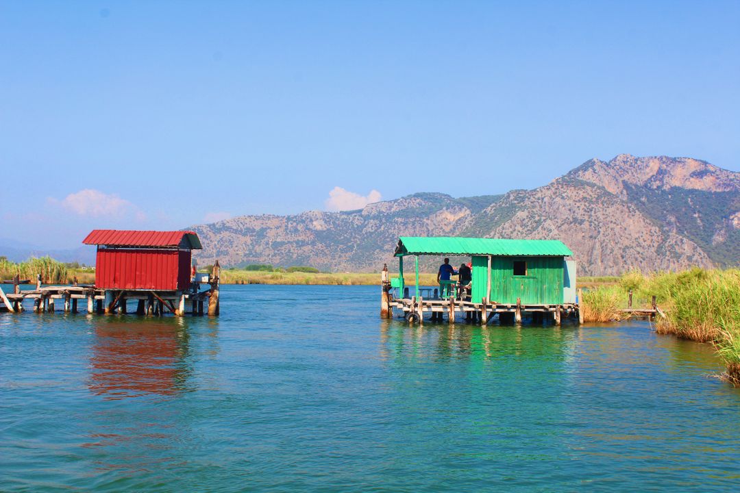 Riverside Huts on Tranquil Lake with Mountain Backdrop - Free Images, Stock Photos and Pictures on Pikwizard.com