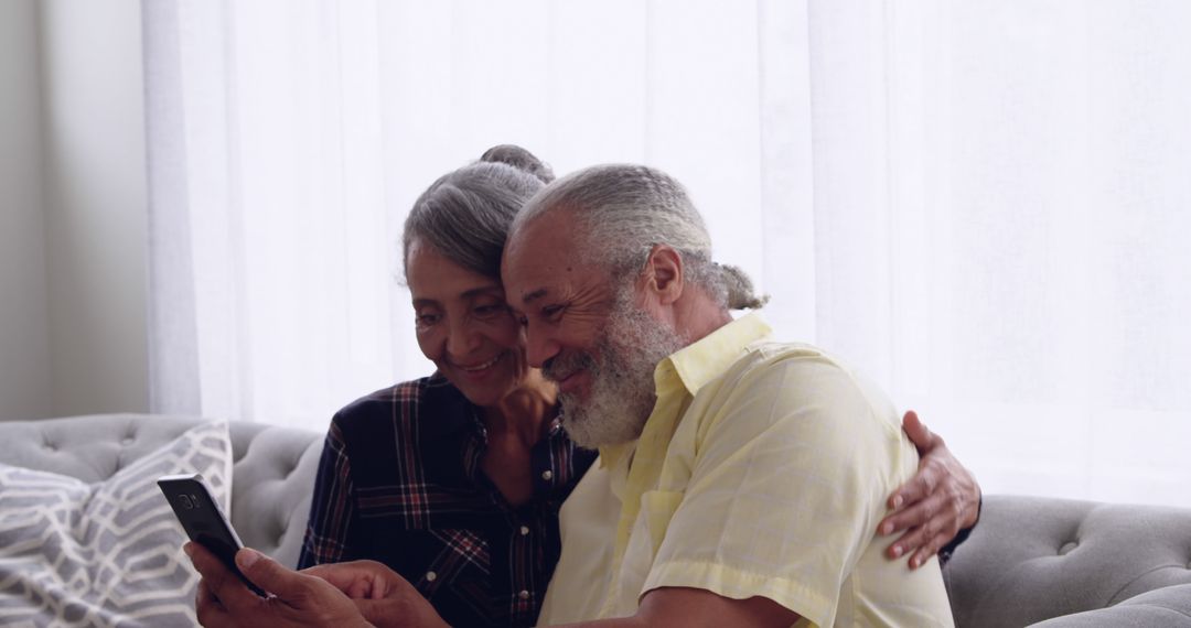 Senior Couple Embracing While Looking at Smartphone at Home