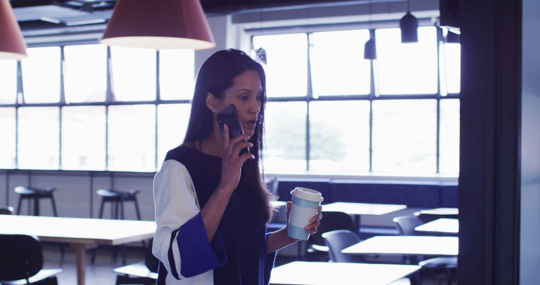 Businesswoman Speaking on Phone While Holding Coffee in Modern Office - Free Images, Stock Photos and Pictures on Pikwizard.com