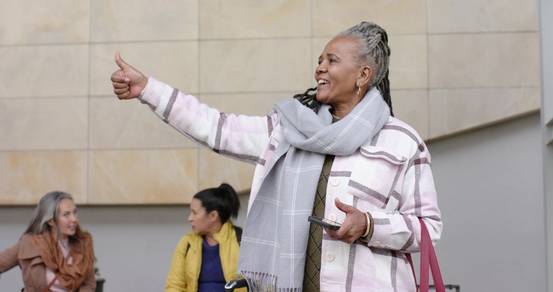 Senior African-American woman giving thumb-up while holding smartphone and waiting in lobby