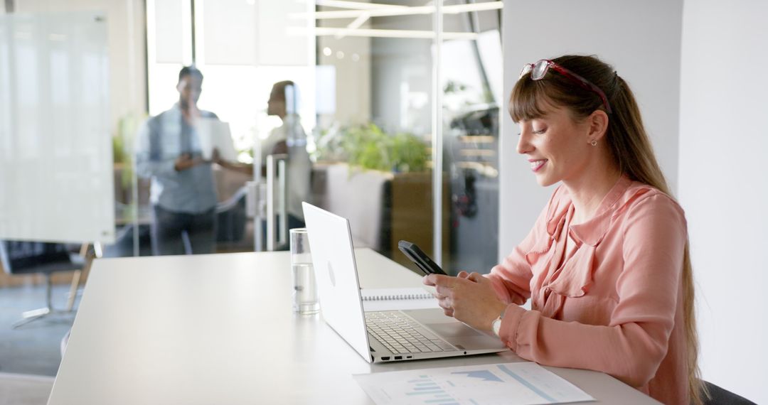 Woman Balancing Smartphone and Laptop Tasks in Modern Office