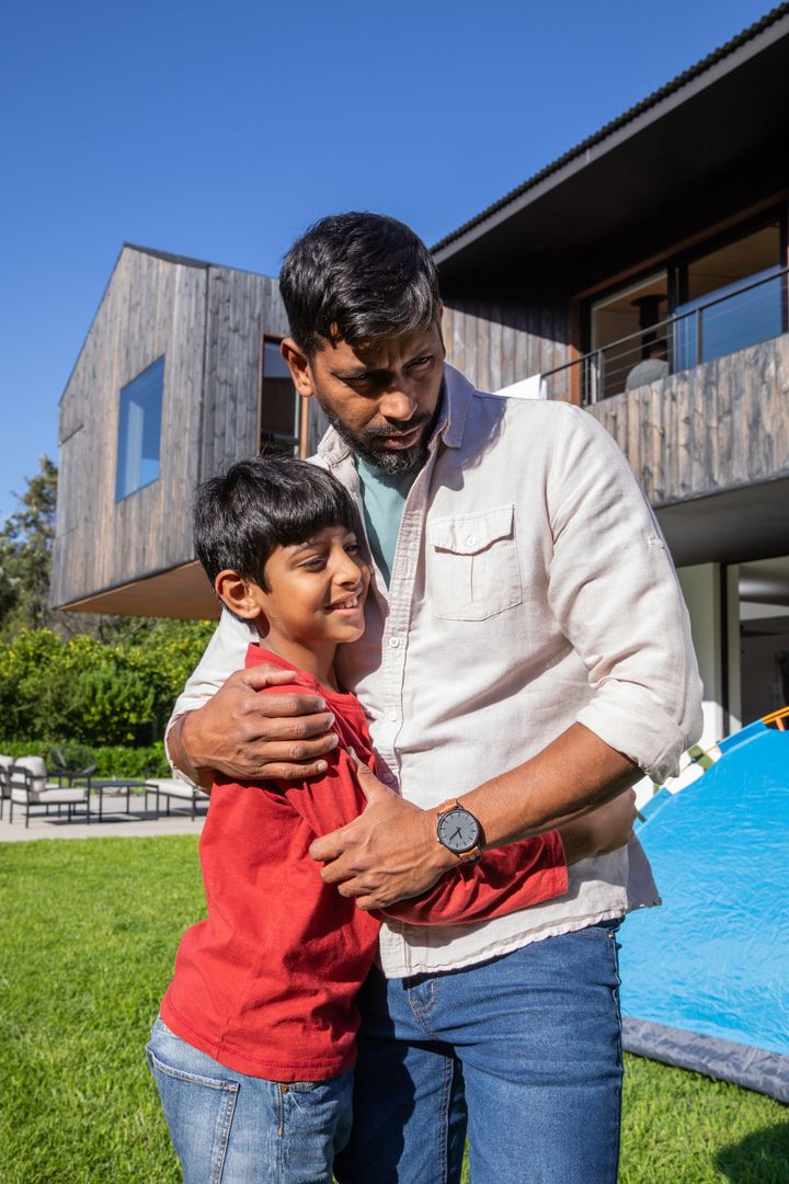 Father and Son Embracing in Front of Modern Home with Tent
