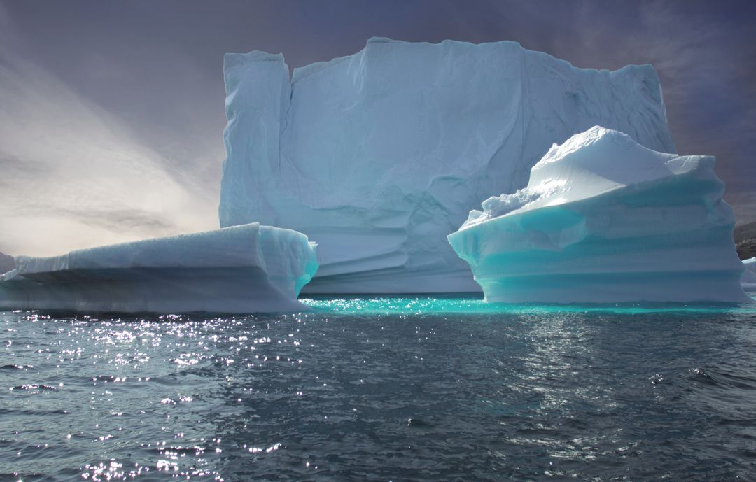 Turquoise Underlit Iceberg Rising from Dark Ocean with Dramatic Moody Sky