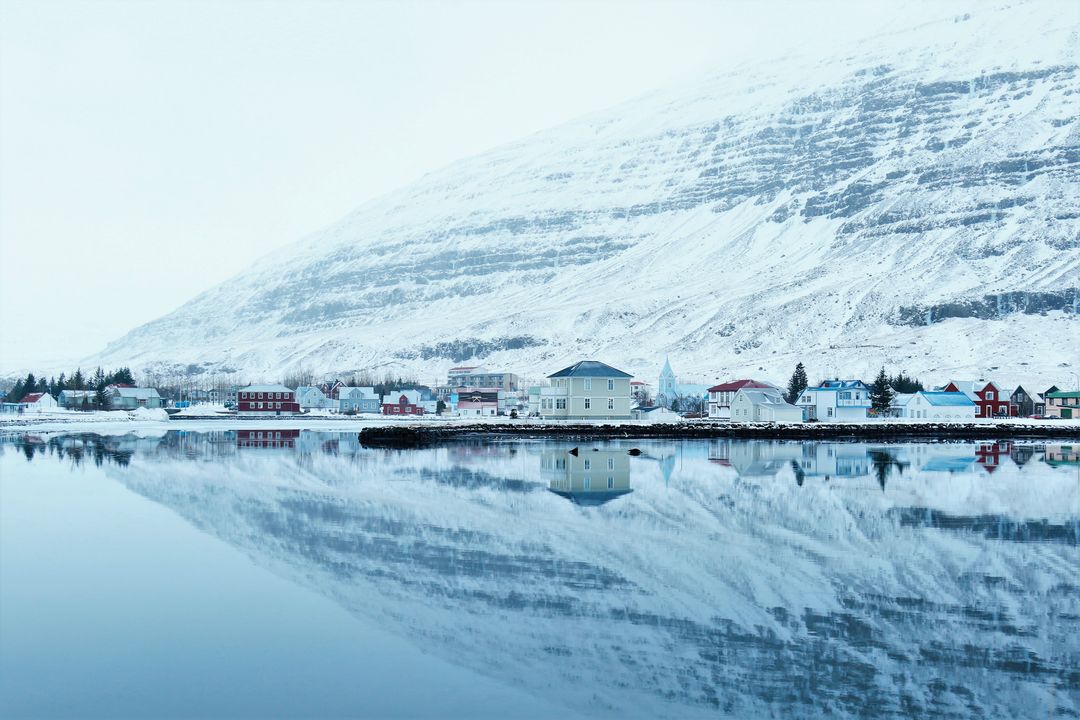 Snow-covered houses reflecting in calm lake against snowy mountain - Free Images, Stock Photos and Pictures on Pikwizard.com