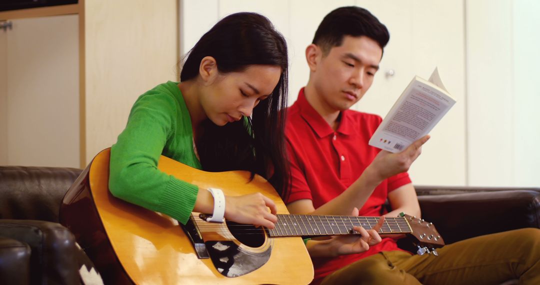 Young Asian couple focusing on playing guitar and reading book at home - Free Images, Stock Photos and Pictures on Pikwizard.com