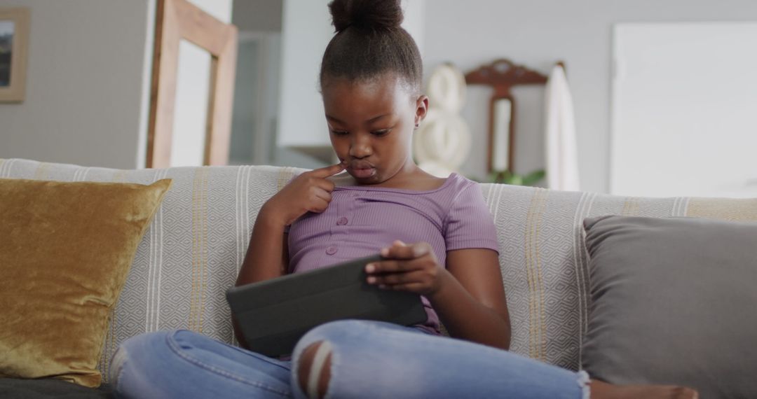 Young girl using tablet while sitting on couch at home - Free Images, Stock Photos and Pictures on Pikwizard.com