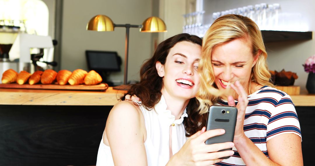 Two Women Laughing and Looking at Smartphone in Coffee Shop - Free Images, Stock Photos and Pictures on Pikwizard.com