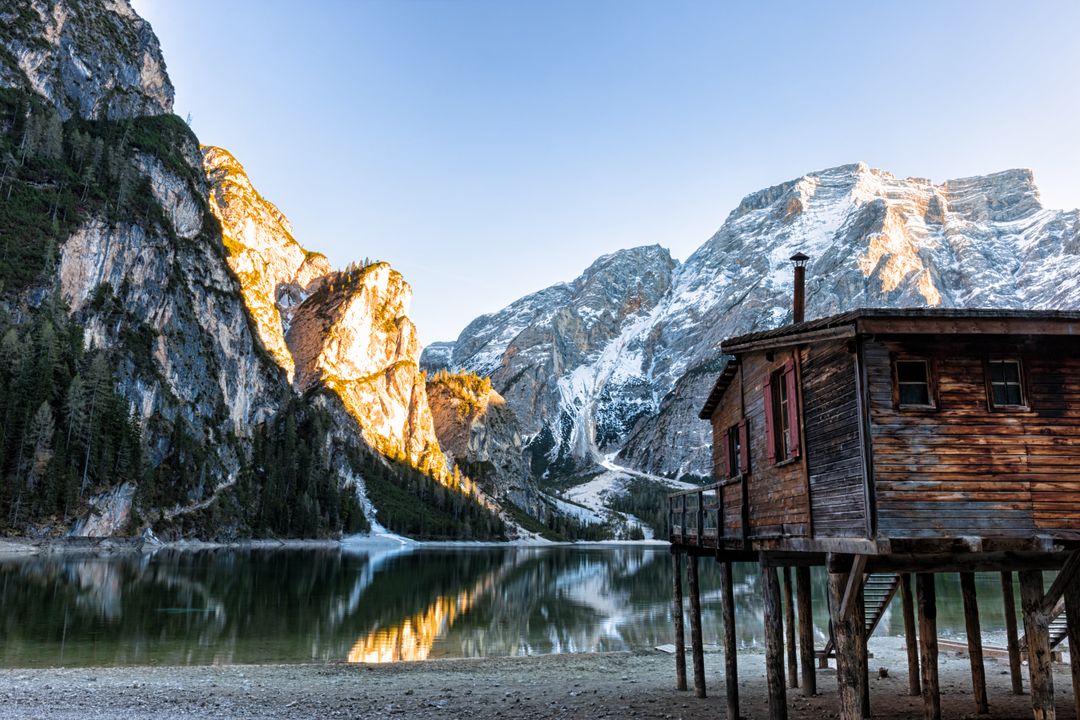 Sunlit Alpine Lake with Rustic Boathouse on Stilts, Snow-Capped Peaks and Reflection