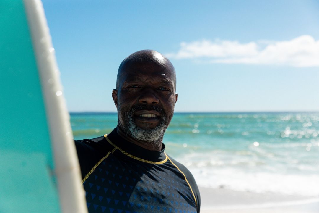 Portrait of african american bald retired senior man standing with surfboard at beach against sky - Free Images, Stock Photos and Pictures on Pikwizard.com