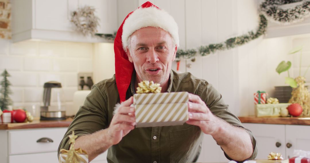 Man With Santa Hat Holding Christmas Gift in Festive Kitchen - Free Images, Stock Photos and Pictures on Pikwizard.com