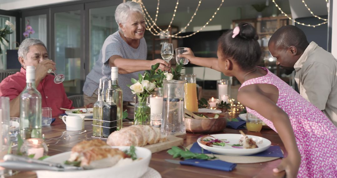Multi-generational family clinking glasses at candlelit dinner table, sharing bread